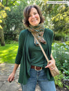 Miik founder Donna (five feet six, small) smiling wearing Miik's Rory waterfall cardigan in pine green with a tank top in the same colour, jeans, scarf and a crossbody purse