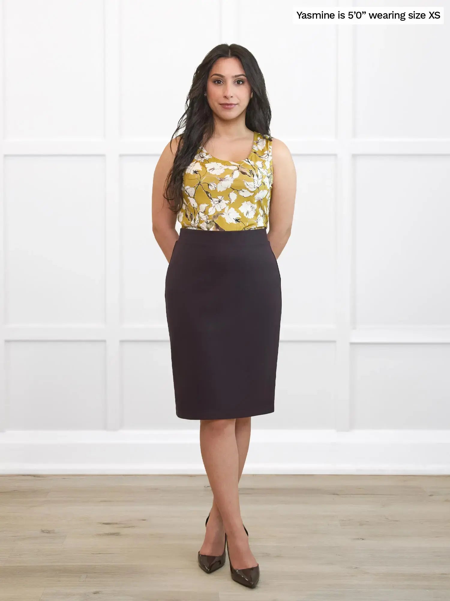Woman wearing a floral top and dark brown skirt against a white background 