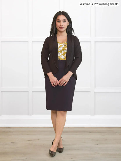Woman wearing a dark brown cardigan and skirt with a yellow blouse featuring floral patterns against a white background 