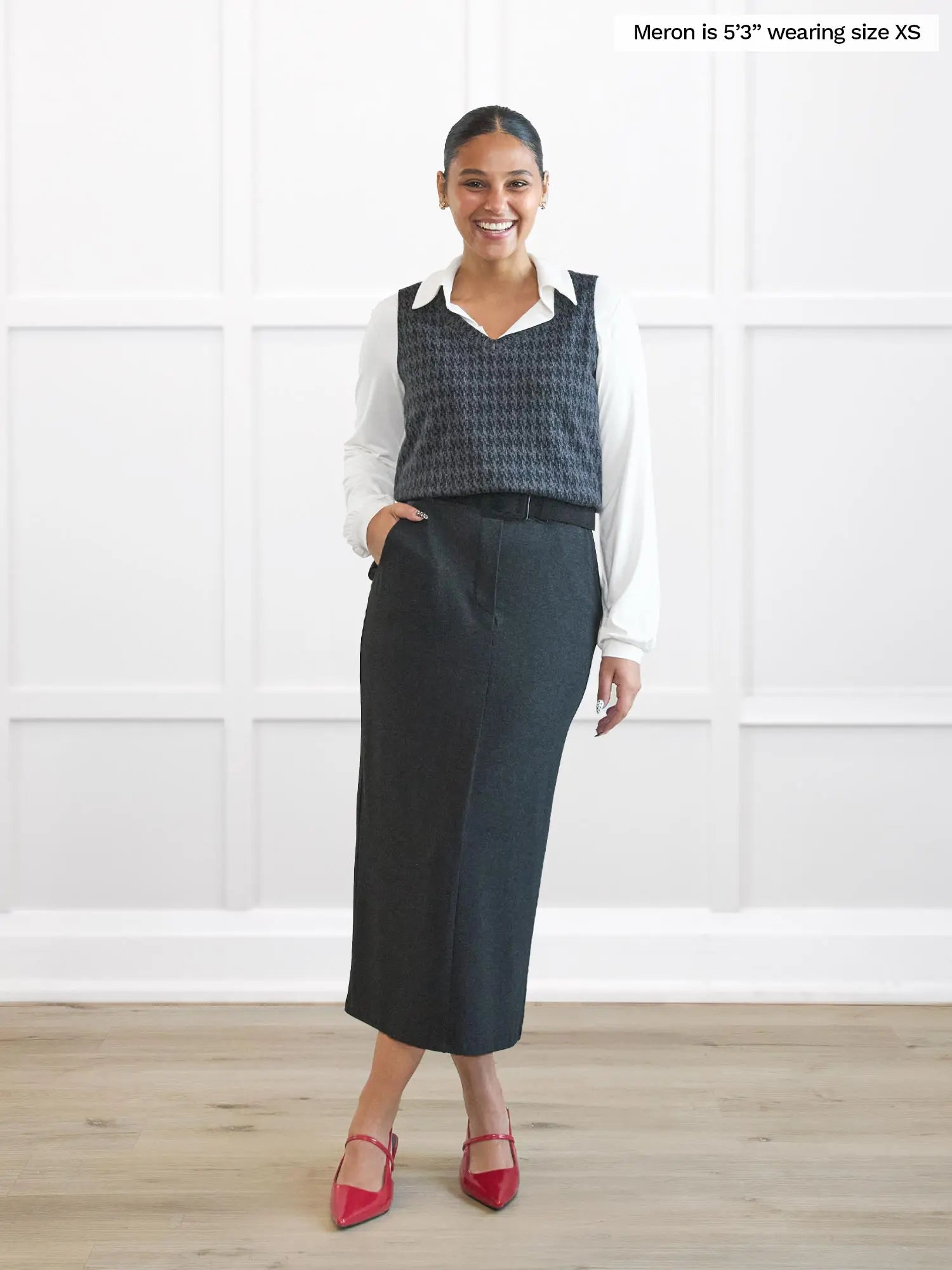 Woman wearing a patterned vest over a white shirt and charcoal skirt on a white background 