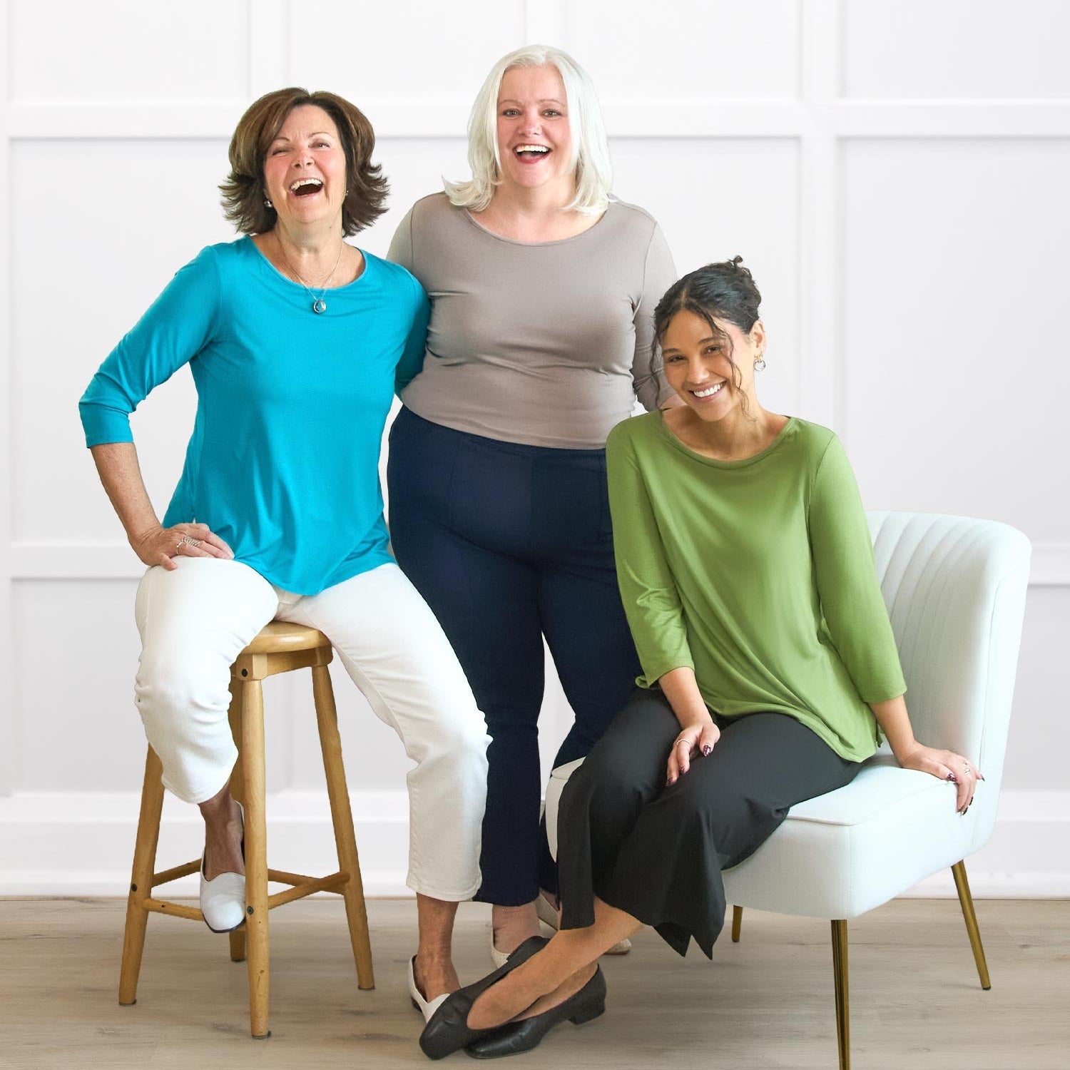 Three women sitting on chairs against a white wall