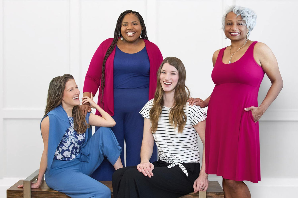 Four women posing together on a bench against a white wall.
