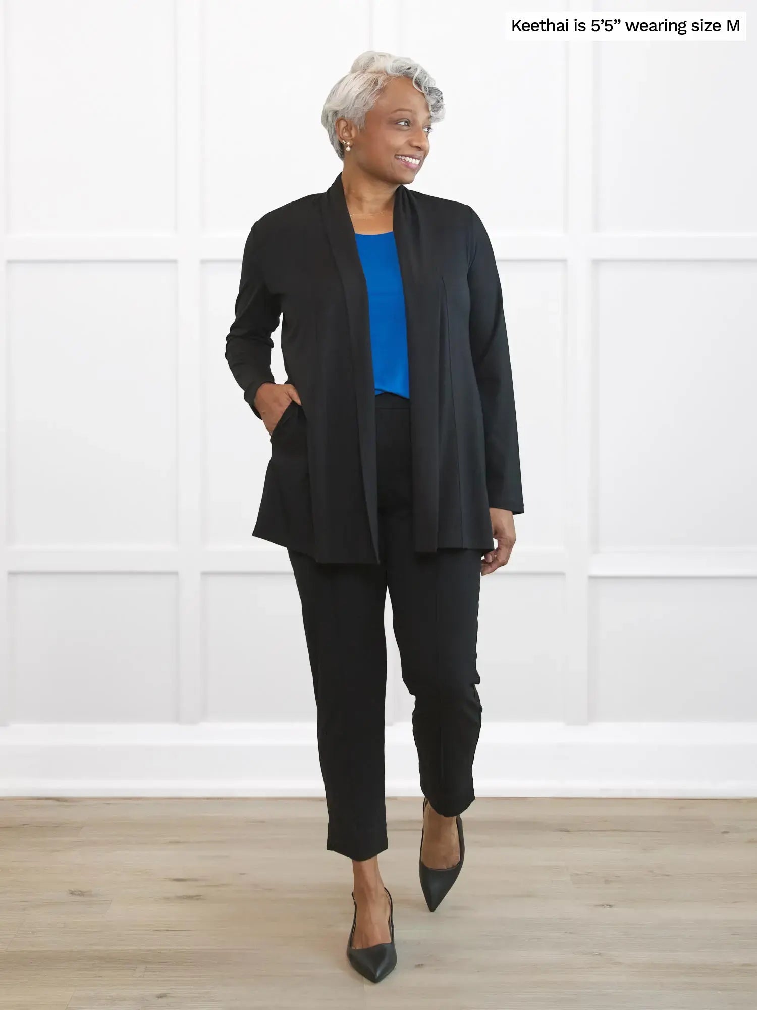 Woman wearing a black suit with a blue top in a room with white walls. 