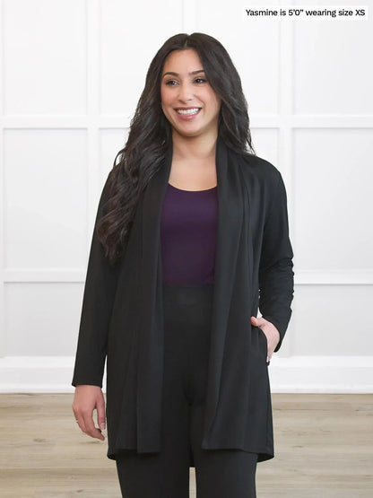 Woman wearing a black cardigan over a purple top and black pants on a white background 