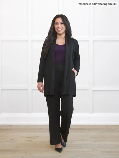 Woman wearing a black suit standing against a white wall. 