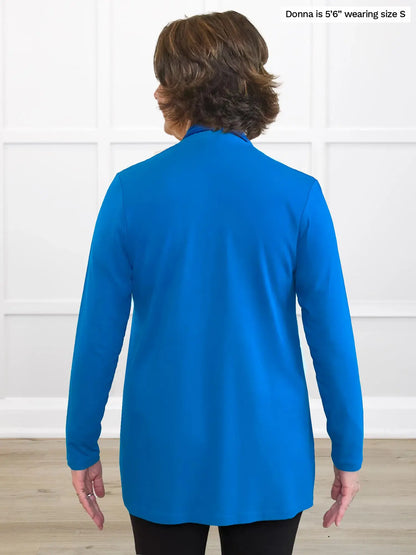 Person wearing a blue cardigan against a white wall 