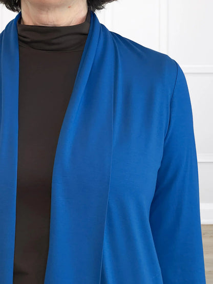 Person wearing a blue cardigan over a brown shirt against a white wall. 