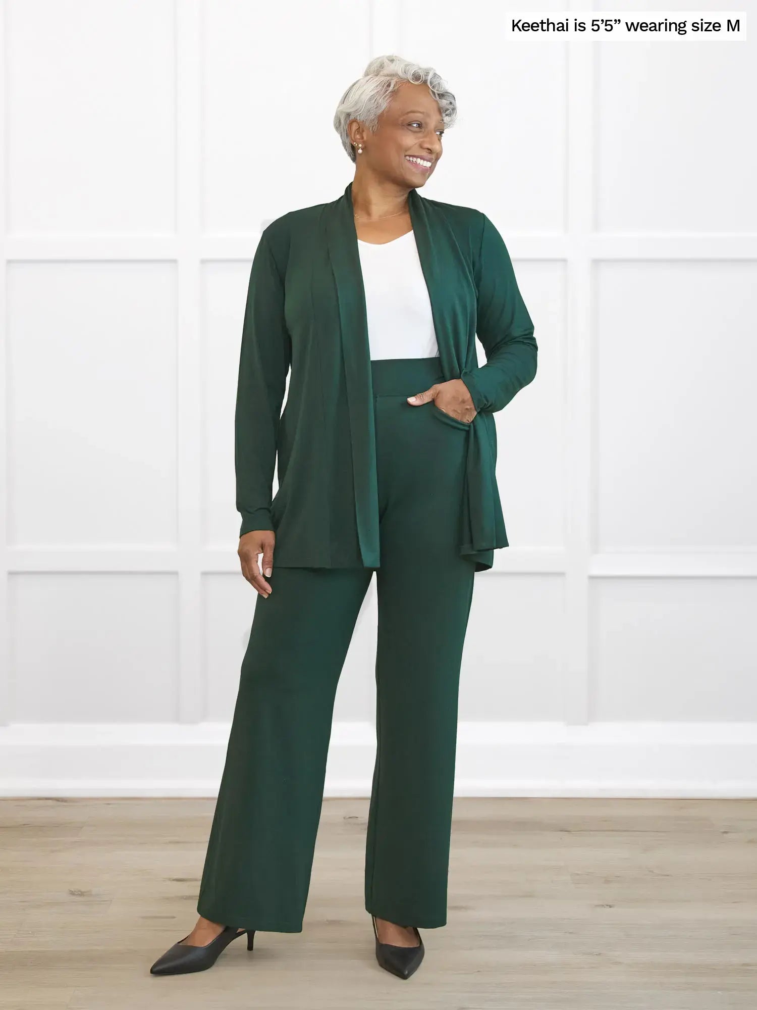 Woman wearing a green suit standing against a white wall. 