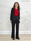 Miik model Lisa (5'6", xsmall) standing in front of a white wall smiling wearing a black straight leg pant, a poppy red tank and Miik's Sade open-front pocket cardigan in black