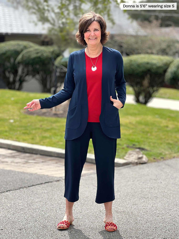 Miik founder Donna (5'6", small) smiling wearing a capri pant in navy with Miik's Sade open-front pocket cardigan in the same colour and a tank top in poppy red