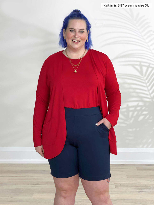 Miik model Kaitlin (5'9", xlarge) smiling wearing a bermuda short in navy with Miik's Sade open-front pocket cardigan in poppy red and a tank top in the same matching colour 