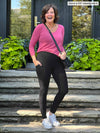 Miik founder Donna (5'6", small) laughing while standing on a outdoor stairs with hands on pockets wearing Miik's Seana high waisted pocket legging in black along with a long sleeve top in pink and white sneakers 