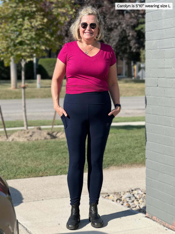A woman standing outside, smiling while wearing the Seana high waisted pocket legging in navy.