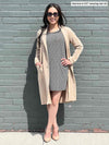 Woman standing in front of a wall wearing Miik's Serena long coat in beige over a dress.