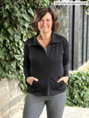 Miik founder Donna (5'6", wears S) smiling wearing Miik's Shaelyn full zip luxe fleece jacket in black with a granite jogger. Donna has sized down the jacket to XS