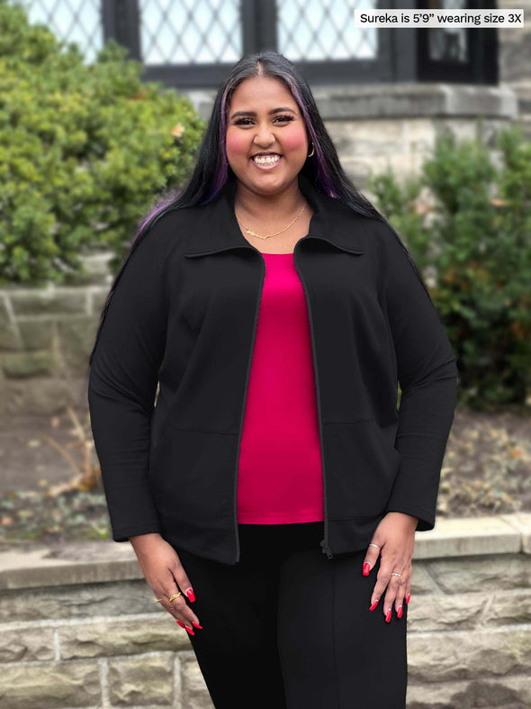 Miik model plus size Sureka (5'9", size 3x) smiling wearing Miik's Shaelyn full zip luxe fleece jacket in black along with a black pant and bordeaux tank top 