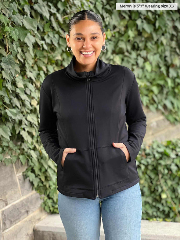 Miik model Meron (5'3", xsmall) smiling wearing Miik's Shaelyn full zip luxe fleece jacket in black with jeans