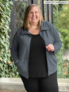 Miik model plus size Jen (5'2", size 3x) smiling wearing an a black tank with legging in the same colour with Miik's Shaelyn full zip luxe fleece jacket in granite 