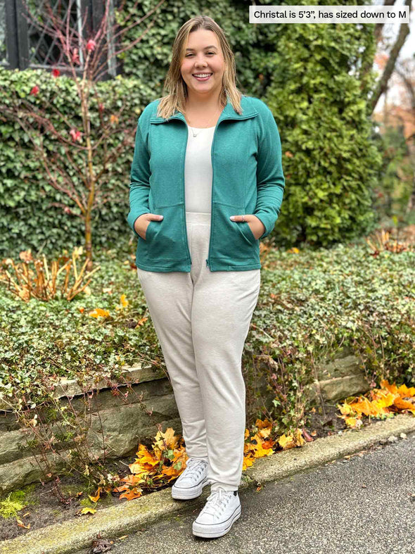Miik model Christal laughing wearing a matching lounge set in oatmeal melange along with Miik's Shaelyn full zip luxe fleece jacket in jade melange green. Christal has sized down the jacket to M