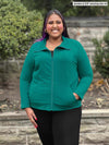Miik model plus size Sureka (5'9", size 3x) smiling wearing Miik's Shaelyn full zip luxe fleece jacket in jade melange zipped up along with a black pant 