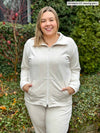 Miik model Christal smiling with hands on pockets wearing Miik's Shaelyn full zip luxe fleece jacket in oatmeal melange along with a jogger in the same matching colour