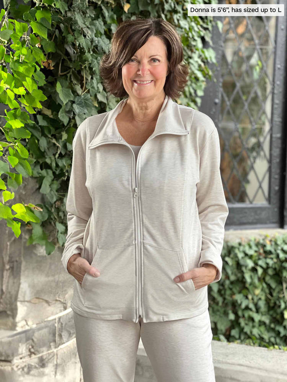 A closeup shot of Miik's founder Donna (5'6", small) smiling wearing a matching fleece set in oatmeal melange with boots. Donna is wearing Miik's Shaelyn full zip luxe fleece jacket along with the Linaya jogger