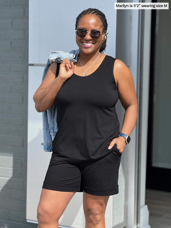 Woman standing in front of a grey wall smiling while wearing Miik's Shandra reversible tank top in black colour.