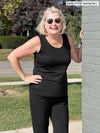 Woman standing by a wall wearing Miik's Shandra reversible tank top in black with black pants.