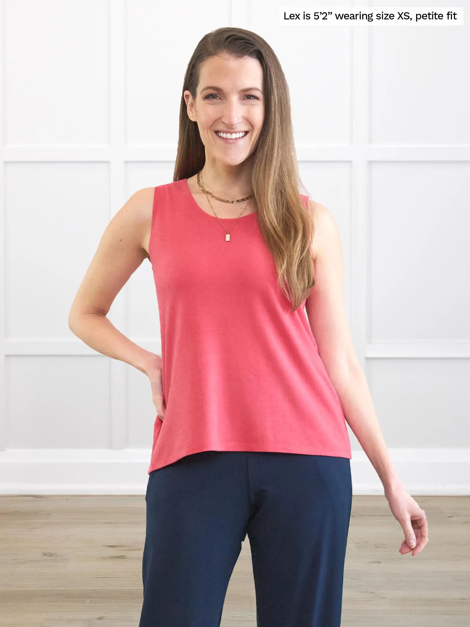 Woman wearing a pink sleeveless top and navy pants in a white room. 