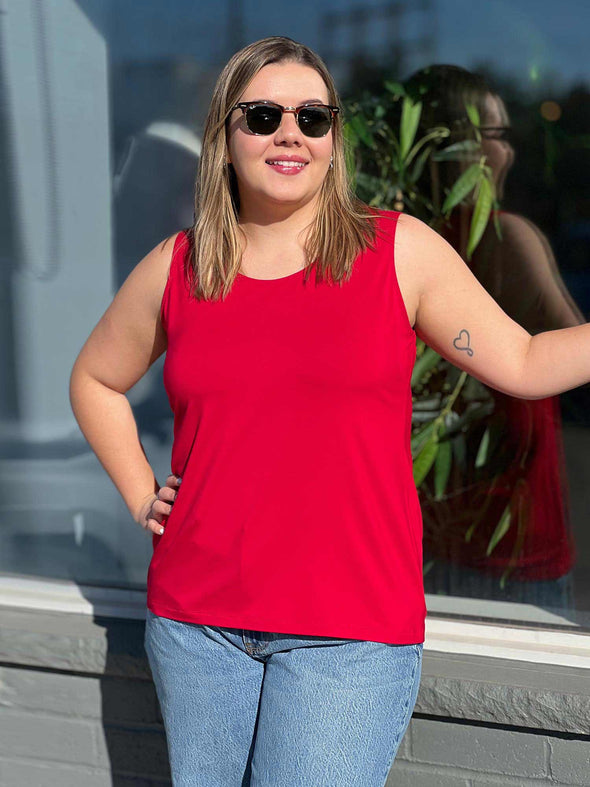 Miik model Christal (5'3, large) smiling and looking away wearing Miik's Shandra reversible tank top in poppy red with jeans and sunglasses 