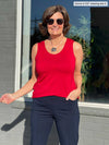 Miik founder Donna (5'6", small) smiling while standing in front of a window wearing a navy pant along with Miik's Shandra reversible tank top in poppy red and sunglasses 