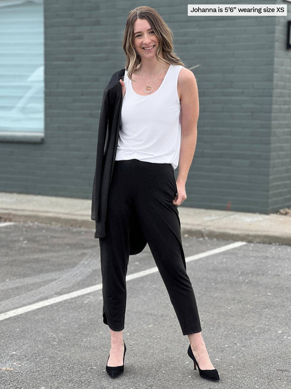 Woman standing in a parking lot smiling while wearing Miik's Shandra reversible tank top in white color with black pants.