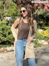 Miik model Johanna (5'6", xsmall) smiling wearing MIik's Shandra reversible tank top in chocolate melange along with a long cardigan in the camel melange colour, jeans and sunglasses 