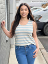 Miik model Yasmine (five feet tall, size extra small, petite) standing next to a brick wall wearing Miik's Shandra reversible tank top in oatmeal mist stripe with jeans