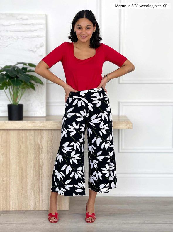 Miik model Meron (5'3", xsmall) smiling while standing in front of a white wall wearing Miik's Shani reversible half sleeve square neck top in poppy red with a printed pant 
