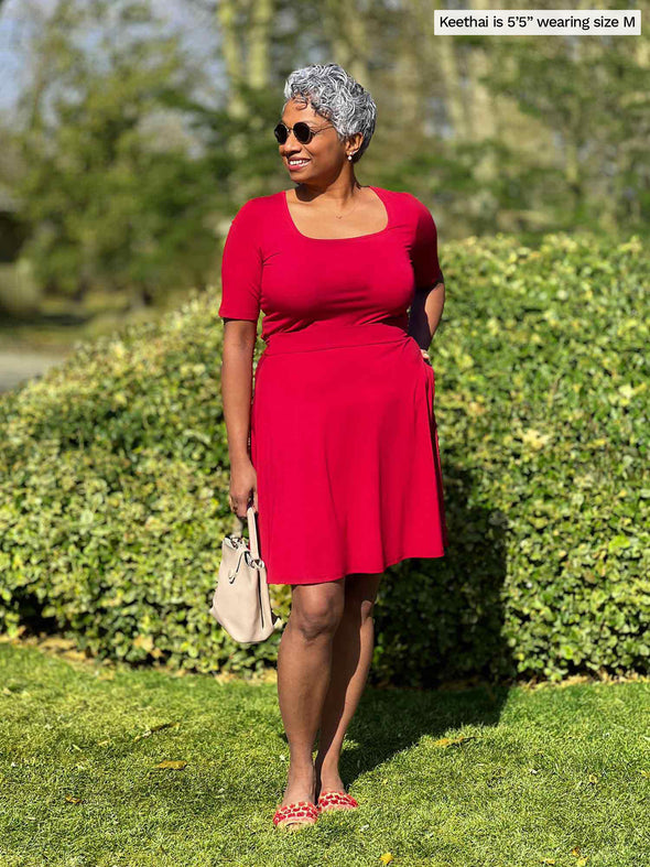 Miik model Keethai (5'5", medium) smiling and looking away wearing Miik's Shani reversible half sleeve square neck top in poppy red along with a skirt in the same colour 