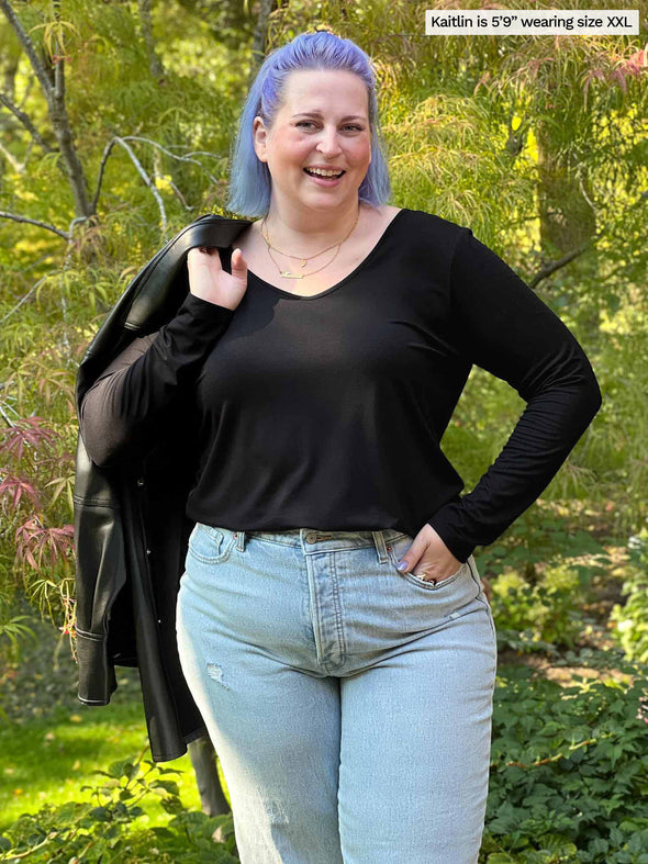 Woman standing in nature wearing Miik's Shannon long sleeve tee in black with blue jeans. 