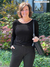Woman standing in nature wearing Miik's Shannon long sleeve tee in black with charcoal pants.
