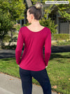 Miik model Johanna, size XS, showing the back of the Shannon long sleeve tee in bordeaux red with navy pants.