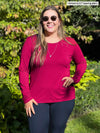 Woman standing in nature wearing Miik's Shannon long sleeve tee in red with navy pants.