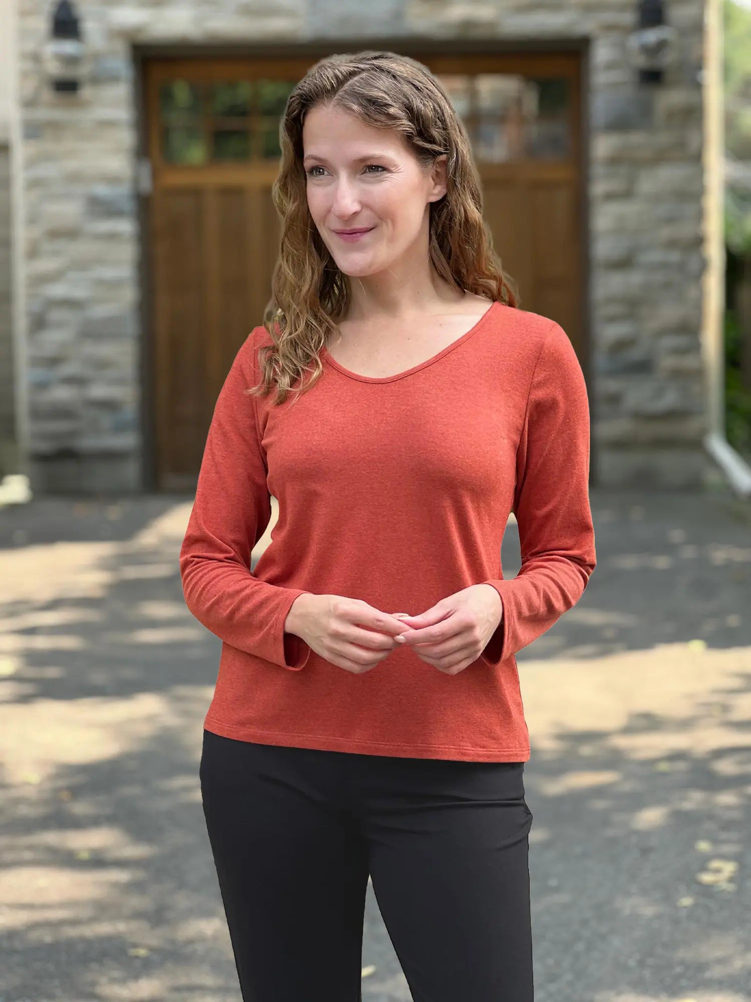 Miik model Lex (size XS) wearing the Shannon long sleeve reversible t-shirt in paprika orange, petite fit, with black pants. 