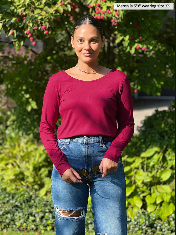 Woman standing in nature wearing Miik's Shannon long sleeve tee in red with jeans.