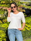 Woman standing in nature wearing Miik's Shannon long sleeve tee in white with jeans. 