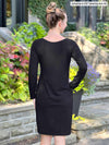 Miik model Johanna (5’6”, xsmall) standing with her back towards the camera showing the back of Miik's Shena long sleeve boatneck pocket dress in black