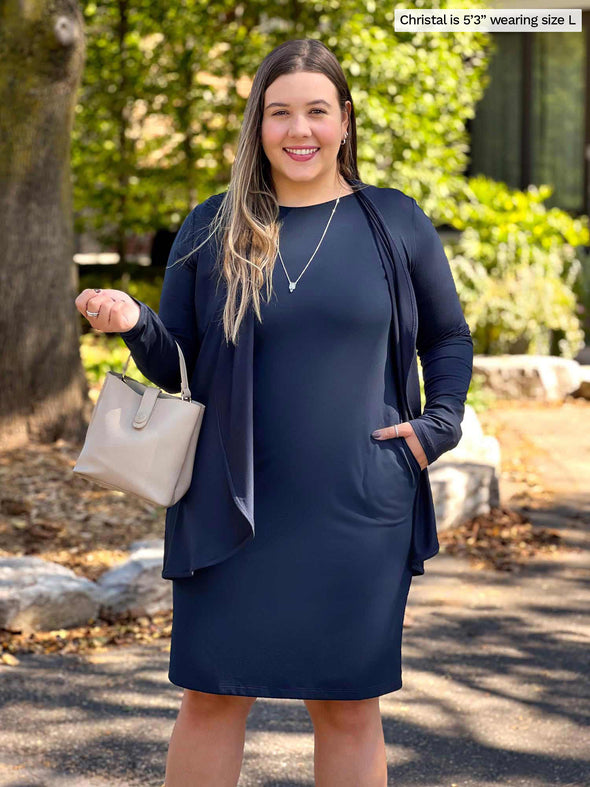 Miik model Christal (5'3", large) smiling wearing Miik's Shena long sleeve boatneck pocket dress in navy with a waterfall cardigan in the same colour 