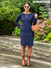 Miik model Meron (5'3", xsmall) with hand on pocket and smiling wearing Miik's Shena long sleeve boatneck pocket dress in navy with brown boots and purse