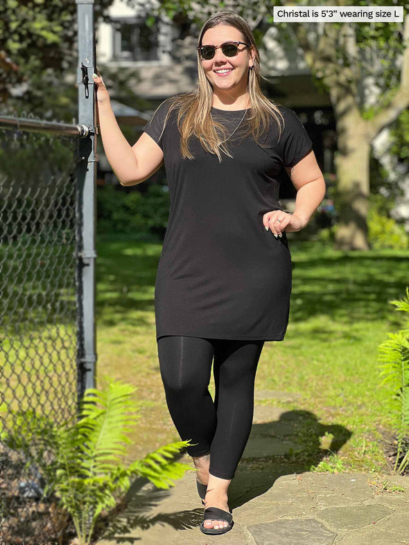 Miik model Christal (5'3", large) standing next to a backyard fence wearing Miik's Sia dolman-sleeve cocoon tunic in black with legging