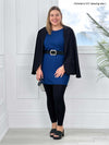 Miik model Christal (5'3", large) smiling while standing in front of a window wearing Miik's Sia dolman-sleeve cocoon tunic in ink blue along with a black legging, belt and a blazer over her shoulders 