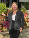 Miik model Christal (5'3", large) smiling wearing Miik's Sienna girlfriend blazer in charcoal with a black pant and a white tank 