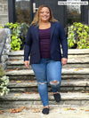 Miik model Carley (5'2", xxlarge) smiling wearing Miik's Sienna girlfriend blazer in navy with a purple top and ripped jeans